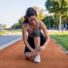 Femme souriante en tenue de sport sur une piste de course, portant une genouillère Orliman Sport pour la protection du genou