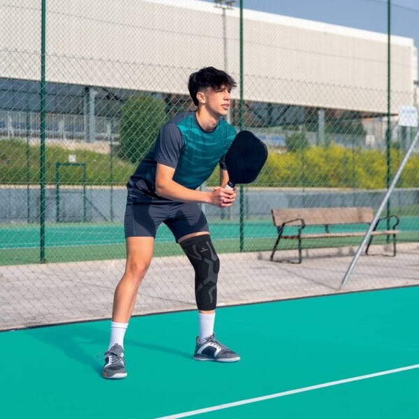 orliman-skintape-genouillere-sit2-1200 Homme jouant au pickleball avec une genouillère Skintape sur terrain extérieur.