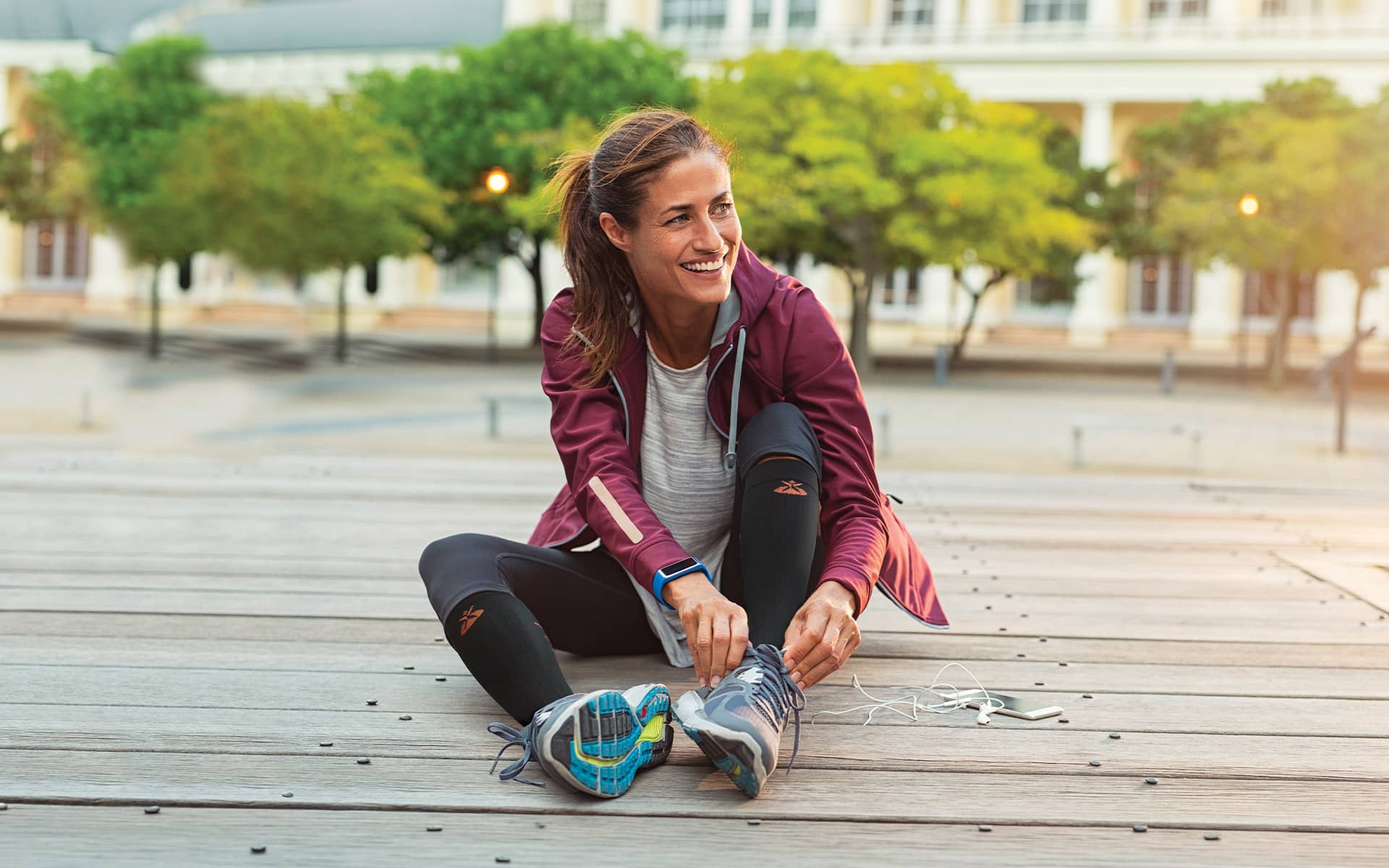 Coureuse souriante qui lace ses chaussures avant l'entraînement et porte des chaussettes de compression Orliman Sport pour optimiser sa récupération