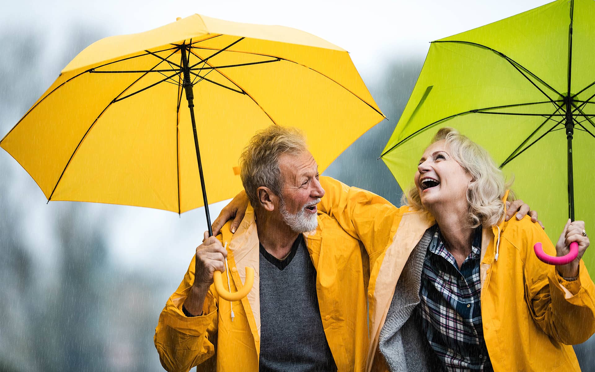 Couple souriant sous la pluie avec parapluies jaune et vert