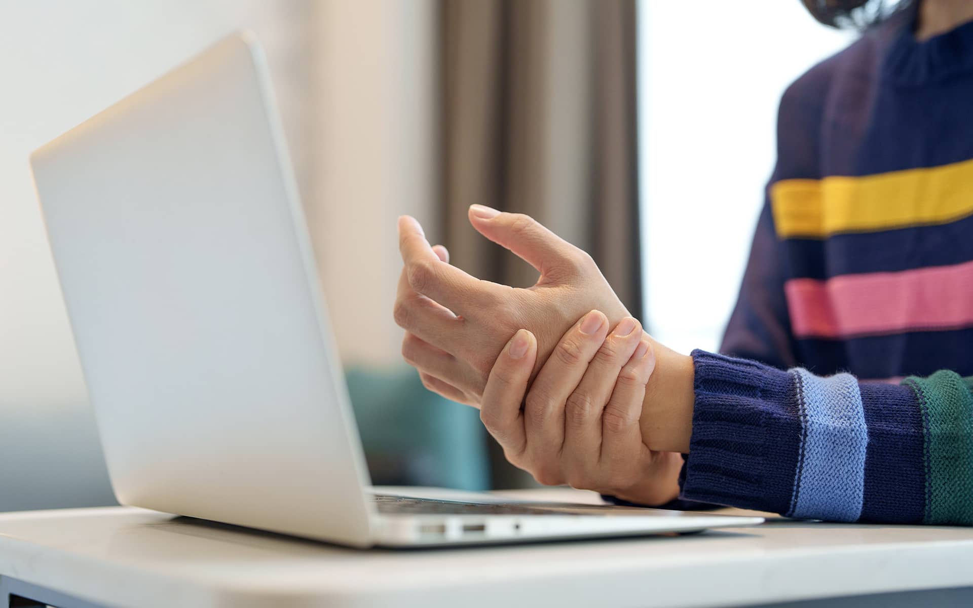 Personne tenant son poignet douloureux devant un ordinateur pour illustrer le syndrome du canal carpien
