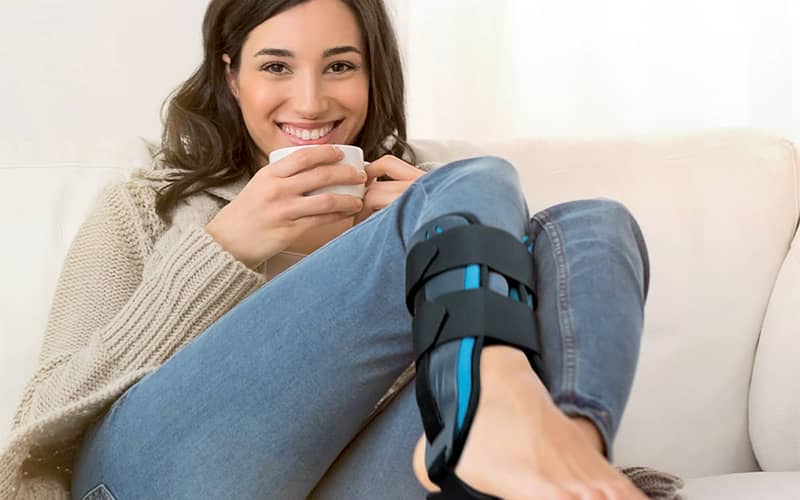 femme souriante sur un canapé avec une attelle de cheville pour entorse