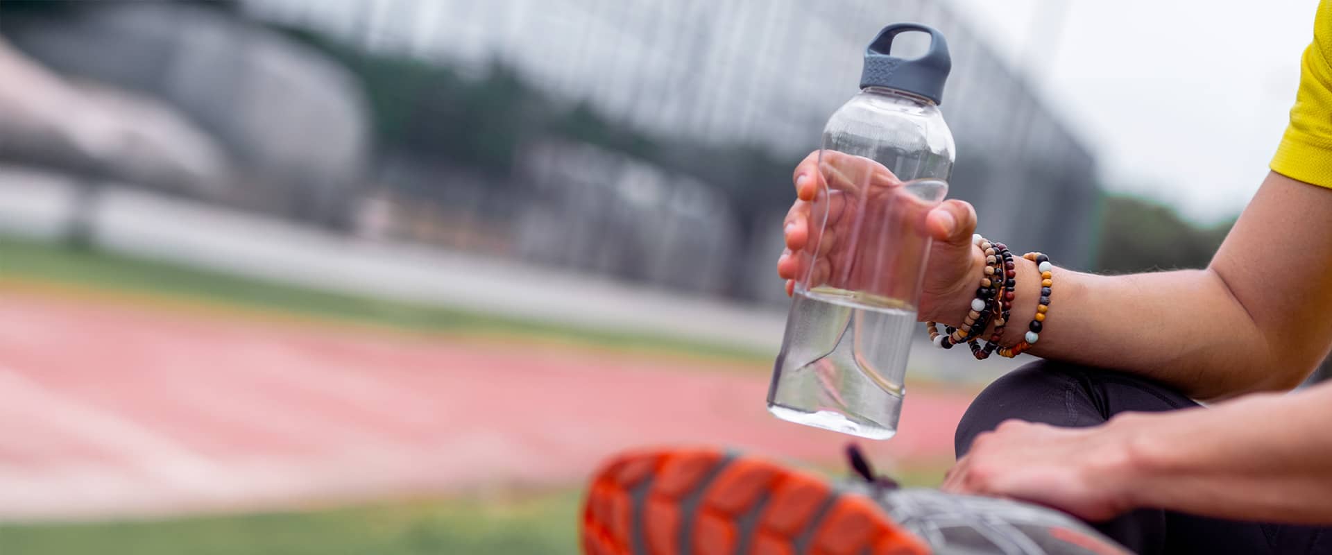 Sportif assis au sol dans un stade tenant une gourde, illustrant l’intérêt de l’hydratation dans la prévention du genou du sauteur.