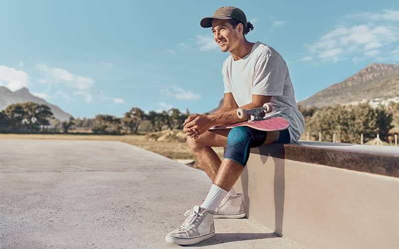 jeune skater assis sur un muret avec son skate sur les genoux et qui porte une genouillère