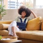 jeune femme souriante assise sur un canapé et portant un bandage d'immobilisation d'épaule
