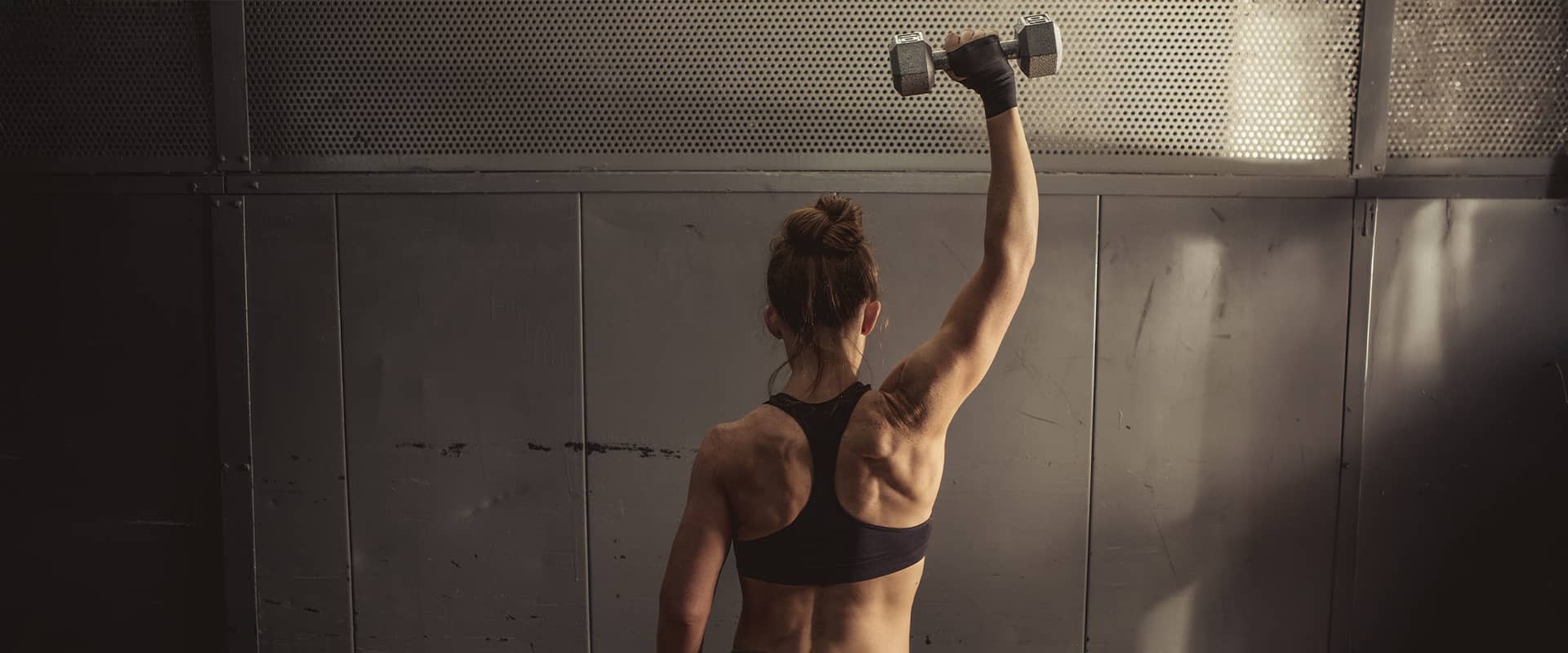 Femme sportive soulevant un haltère en salle de musculation, activité à risque de lésions musculaires et de claquages