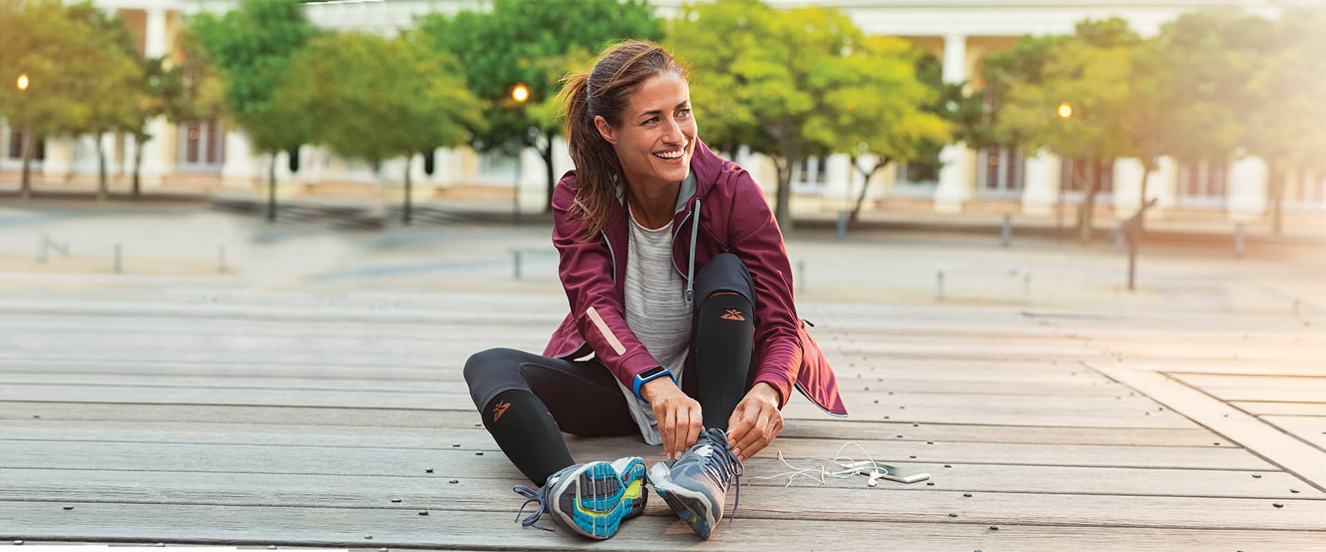 Coureuse souriante qui lace ses chaussures avant l'entraînement et porte des chaussettes de compression Orliman Sport pour optimiser sa récupération