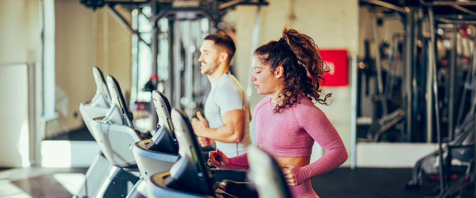 Deux sportifs s'entraînant sur tapis de course en salle de sport, symbole d'un entraînement régulier pour améliorer ses performances physiques