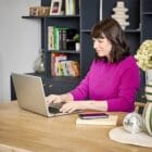 Femme assise à son bureau face à son ordinateur et portant les gants de confort Prim’Arthrose pour soulager les douleurs liées à l’arthrose débutante des doigts