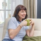 Femme souriante assise dans son canapé avec l'orthèse souple de pouce Prim’Arthrose pour soulager les douleurs liées à la rhizarthrose débutante