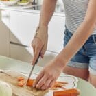 Femme dans sa cuisine qui découpe une carotte et porte l'orthèse souple de pouce Prim’Arthrose pour soulager les douleurs liées à la rhizarthrose débutante